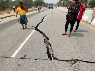 People look at a damaged road on the Naypyidaw-Yangon highway after an earthquake